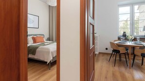 Una habitación con cama, una mesa de comedor con sillas y un ventanal con persianas.