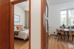 A room with a bed, a dining table with chairs, and a window with blinds. - Charming Apartment in the City Center | Crib and High Chair (Gdańsk)