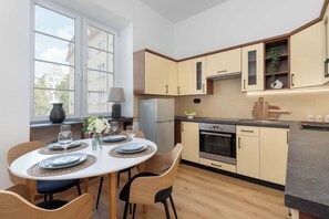 A modern kitchen with a dining area, featuring a large window, built-in cabinets, and a central island. - Charming Apartment in the City Center | Crib and High Chair (Gdańsk)