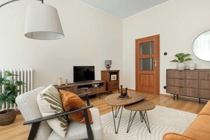 A modern living room with a sofa, TV, wooden cabinet, and a dining table. - Charming Apartment in the City Center | Crib and High Chair (Gdańsk)