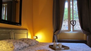 Een hotelkamer met een bed, een nachtkastje met een lamp, een raam met gordijnen en een dienblad met kopjes en een tijdschrift.