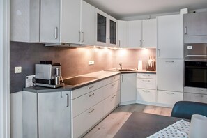 Una cocina moderna con armarios blancos, horno empotrado y cafetera.