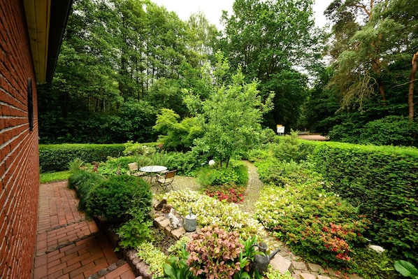 Un jardin avec un mur en briques, un chemin pavé et diverses plantes et fleurs.
