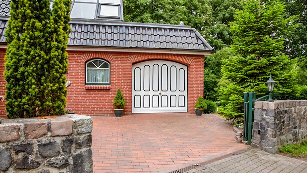 Et murstenshus med stor hvid garageport, et lille vindue og en potteplante.