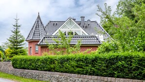 Et hus med en markant taghældning, en murstens skorsten og en stenvæg i forgrunden.