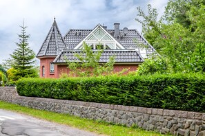 Ein Haus mit steilem Dach, einem Ziegelkamin und einer Steinmauer im Vordergrund.