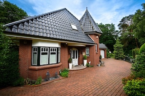 Ein Backsteinhaus mit einem steilen Dach, einer Veranda und einer Auffahrt aus Backsteinen.