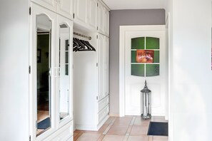 Un pasillo con una puerta blanca, un perchero, un cuadro enmarcado y una lámpara de pie.
