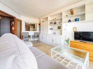 Ein Wohnzimmer mit einer Couch, einem Glastisch, einem Fernseher und einer Schrankwand mit Regalen.