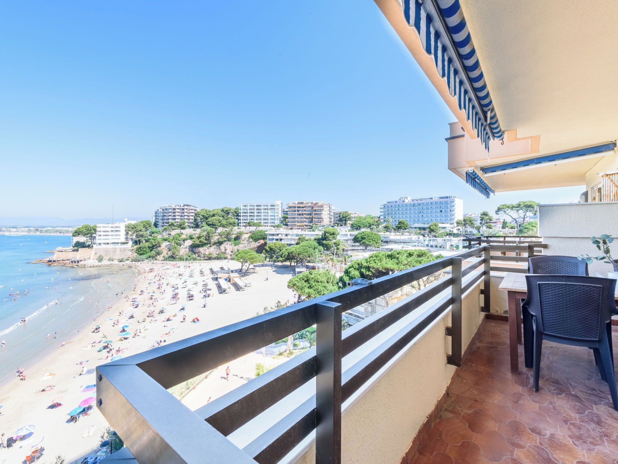 A balcony with a view of a beach, a dining area with chairs, and a tiled floor.