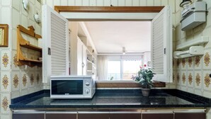 Et køkken med en mikrobølgeovn, skabe, en potteplante og udsigt til en balkon.