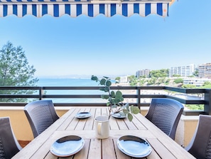 Ein Holztisch mit Tellern, einer Tasse und einem Topf mit Pflanze, mit Blick auf Meer und Häuser.