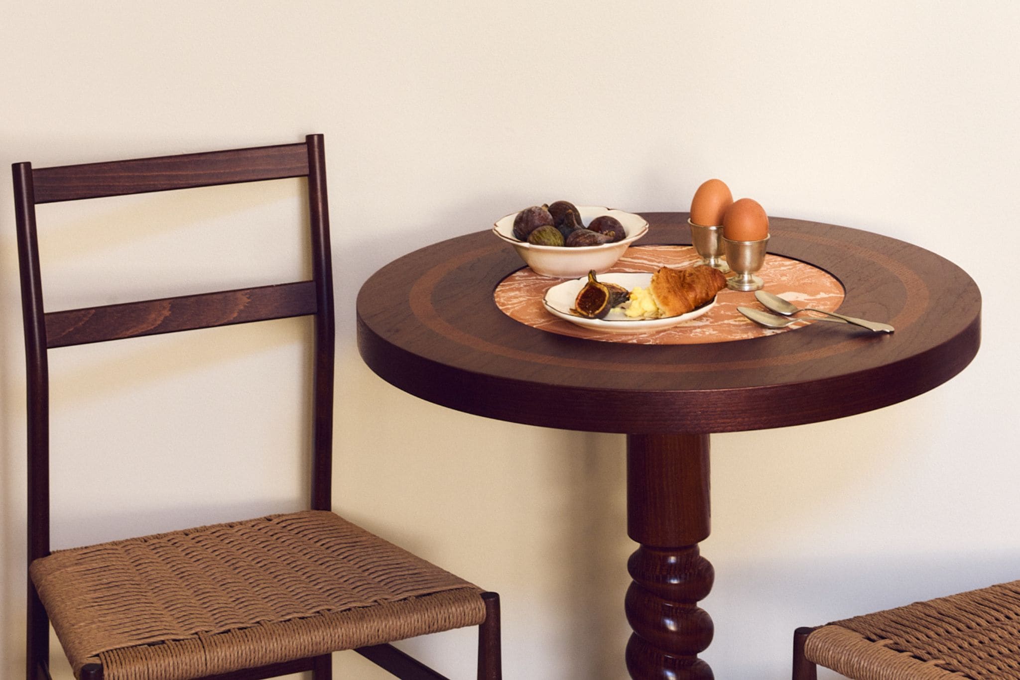 A round wooden table with a plate of food, two eggs, and a bowl of figs.