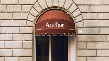 Fachada de edificio con pared de ladrillo, toldo marrón con la palabra 'Anchor' sobre una puerta de vidrio de entrada.