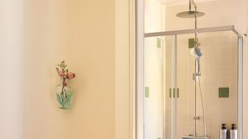 A bathroom with a glass shower enclosure, a vase with flowers on the wall, and toiletries on the shower wall.