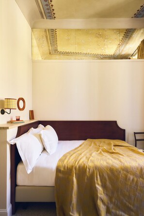 Ett hotellrum med en säng, ett sängbord, en lampa och en tavla som hänger på väggen.