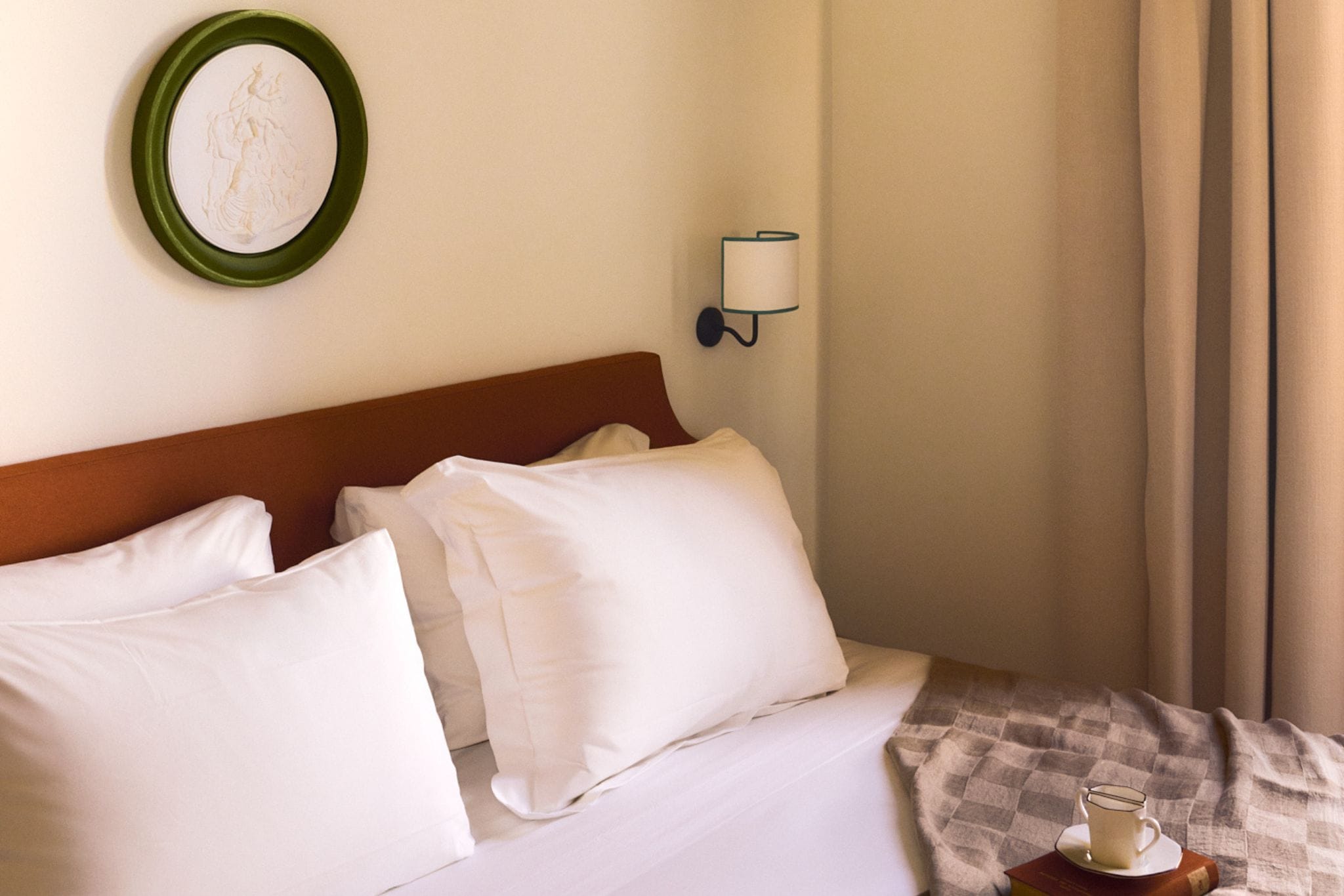 Une chambre d’hôtel avec un lit, des oreillers, une lampe fixée au mur et un tableau encadré.