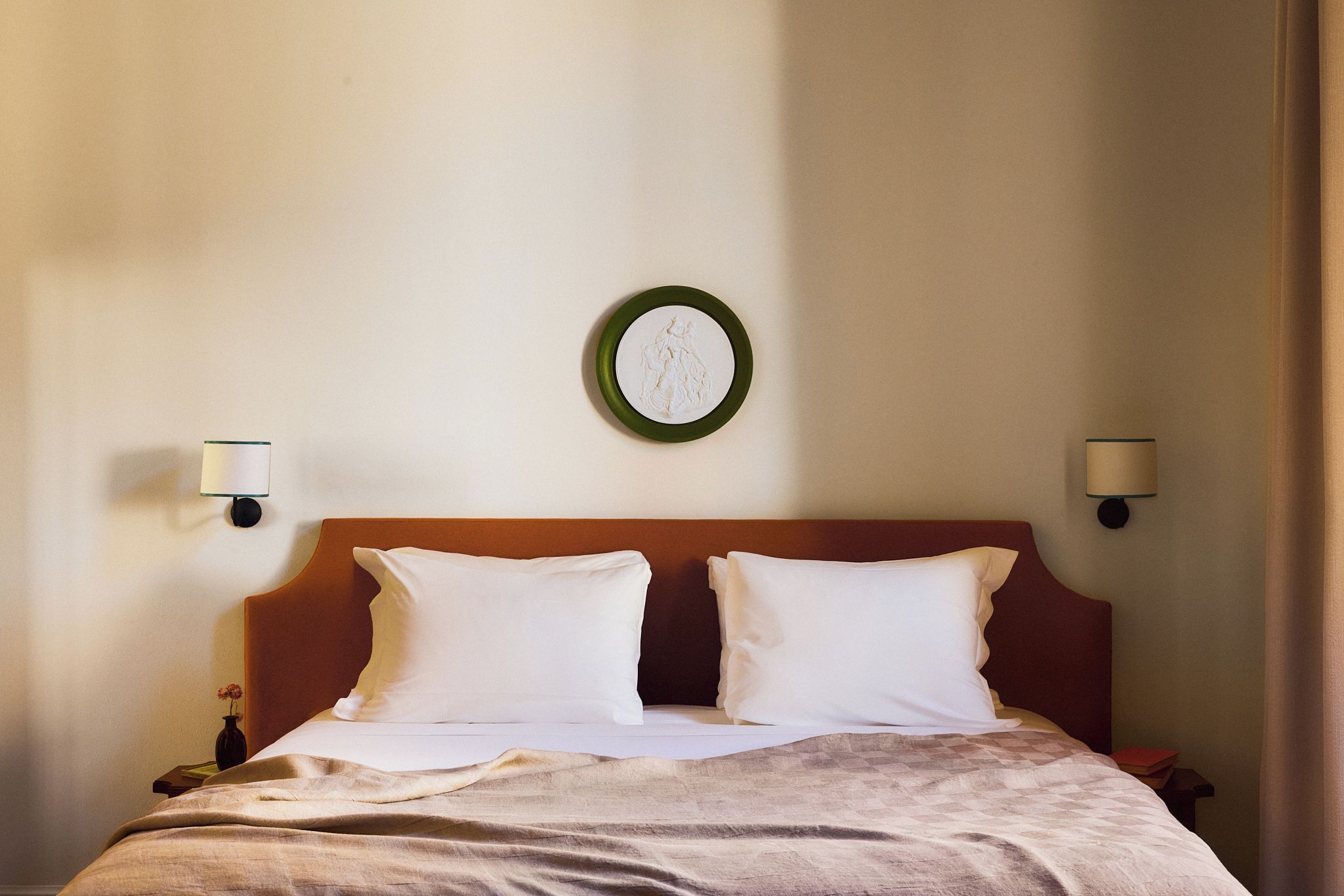 Una habitación de hotel con una cama, dos lámparas de pared y un adorno en la pared.