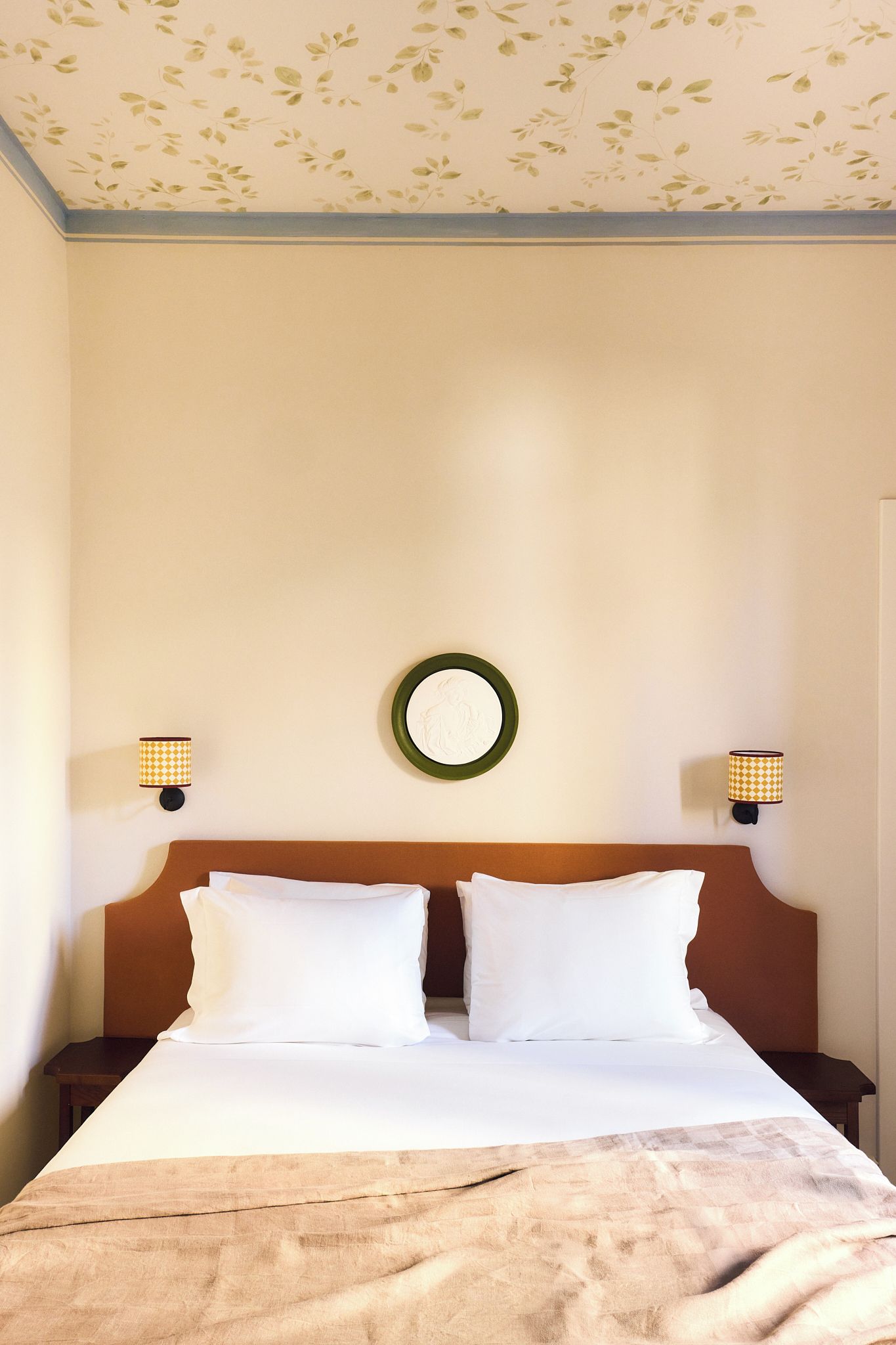 A hotel room with a bed, two wall-mounted lamps, and a circular wall decoration.