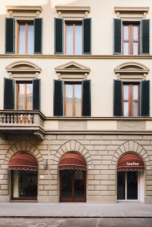 A building with multiple windows, a balcony with balustrade, and storefronts with awnings. - Anchor Santa Croce (Firenze)
