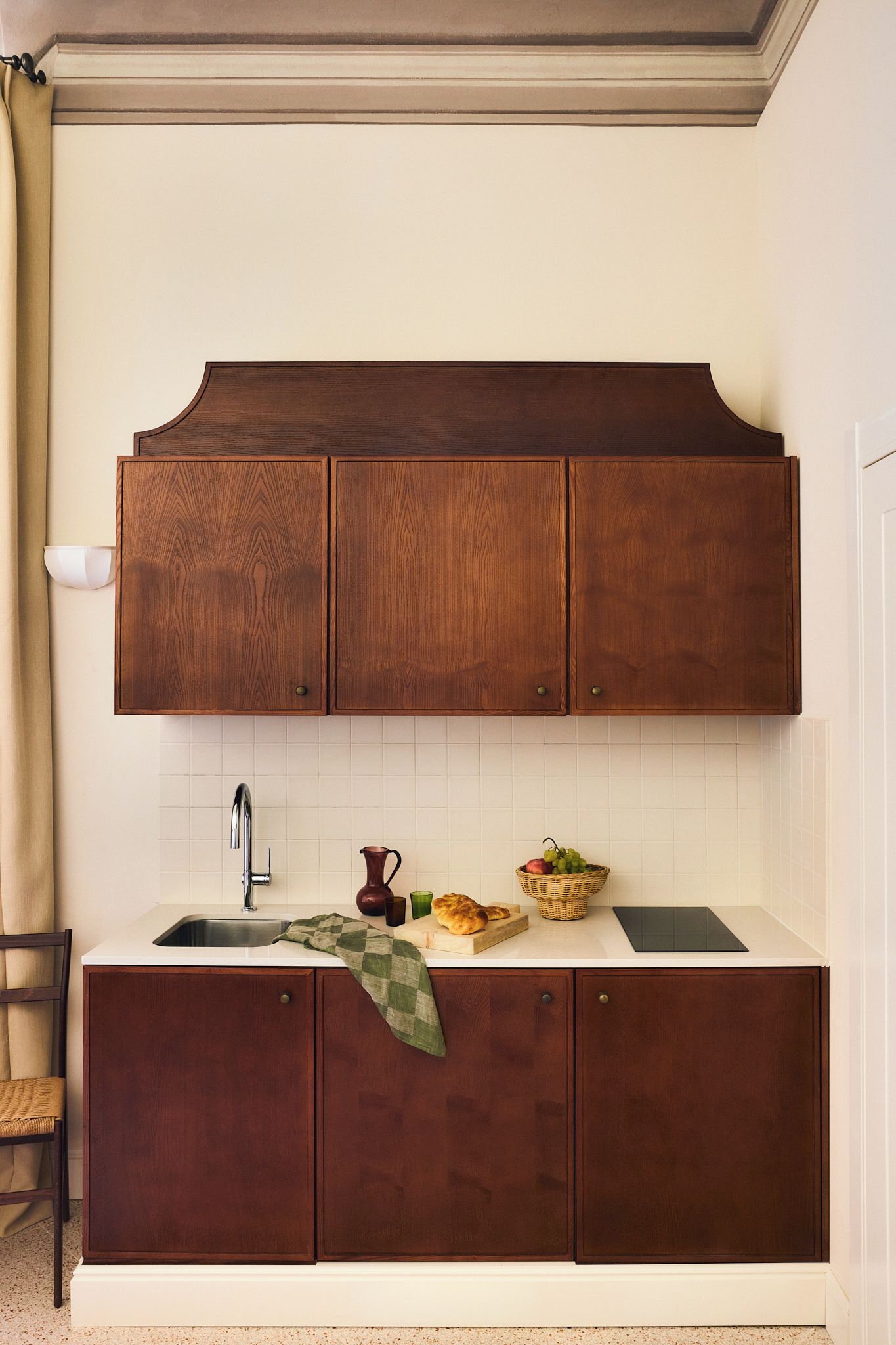 A kitchen with wooden cabinets, a sink, a countertop, and a chair.