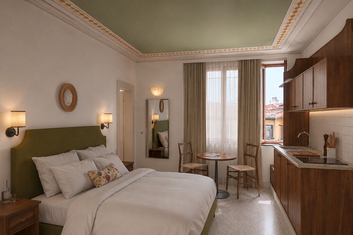 Une chambre d’hôtel comprenant un lit, des tables de chevet, une petite table ronde avec des chaises, un miroir, une fenêtre avec des rideaux et un coin cuisine.