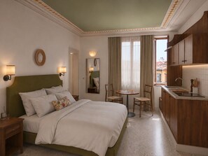 A hotel room with a bed, bedside tables, a small round table with chairs, a mirror, a window with curtains, and a kitchenette area. - Anchor Santa Croce (Firenze)