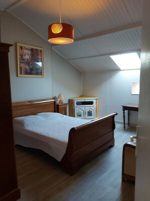 A bedroom with a wooden bed, a nightstand, a dresser, a desk, and a skylight.