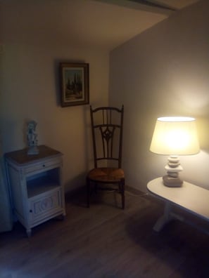 A room with a wooden chair, a small table with a lamp, a cabinet, and a framed picture on the wall.