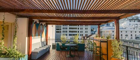 Un espacio de estar al aire libre cubierto, con piso de madera, una mesa y sillas.