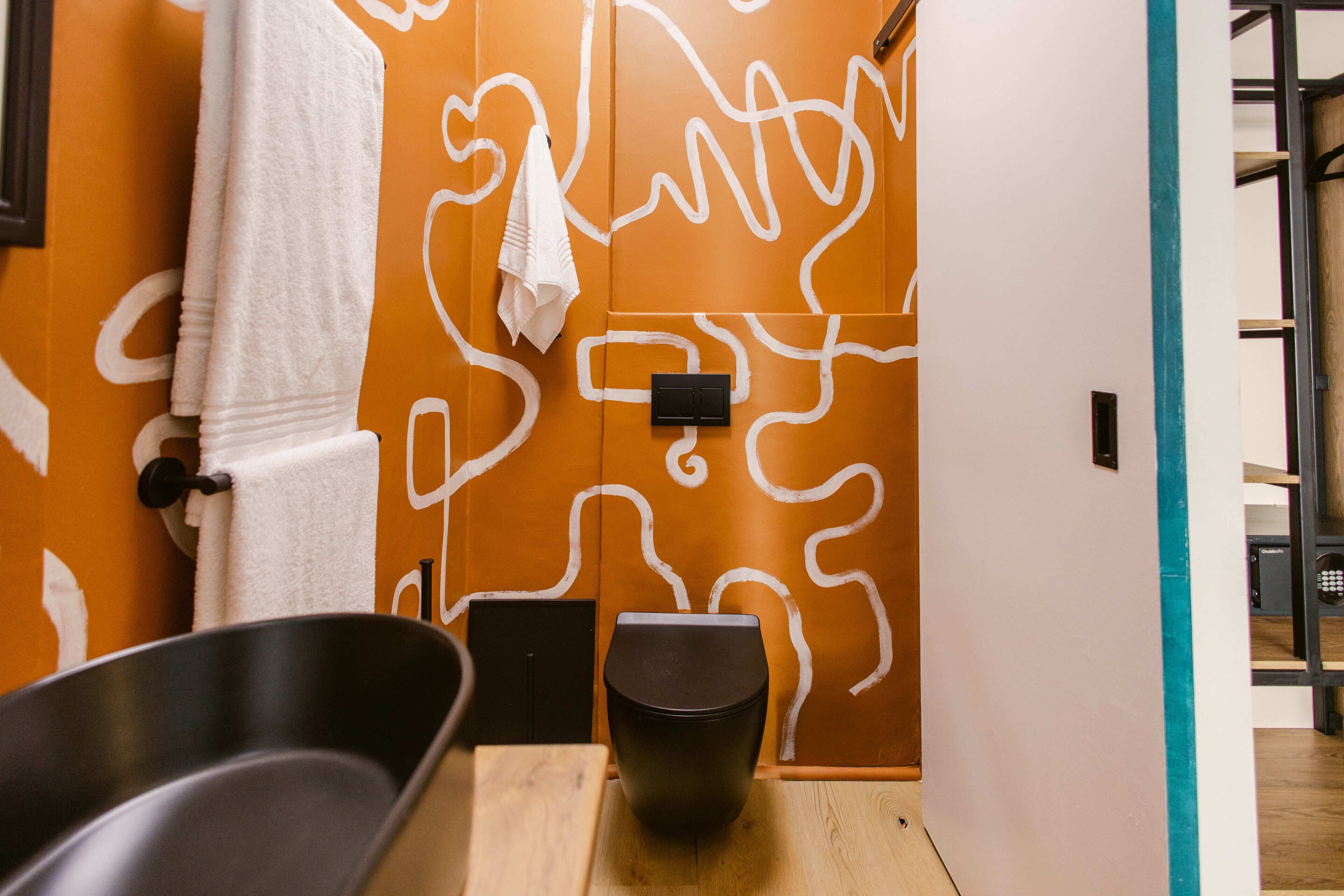 A bathroom with a wooden floor, a black basin, a black toilet, and a towel hanging on a towel rack.