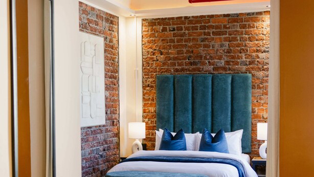 Una habitación de hotel moderna con pared de ladrillo, una cama grande con ropa de cama azul y suelo de madera.
