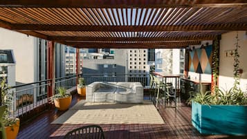 Un balcone con una pergola in legno, posti a sedere all'aperto, piante in vaso e vista sugli edifici della città.