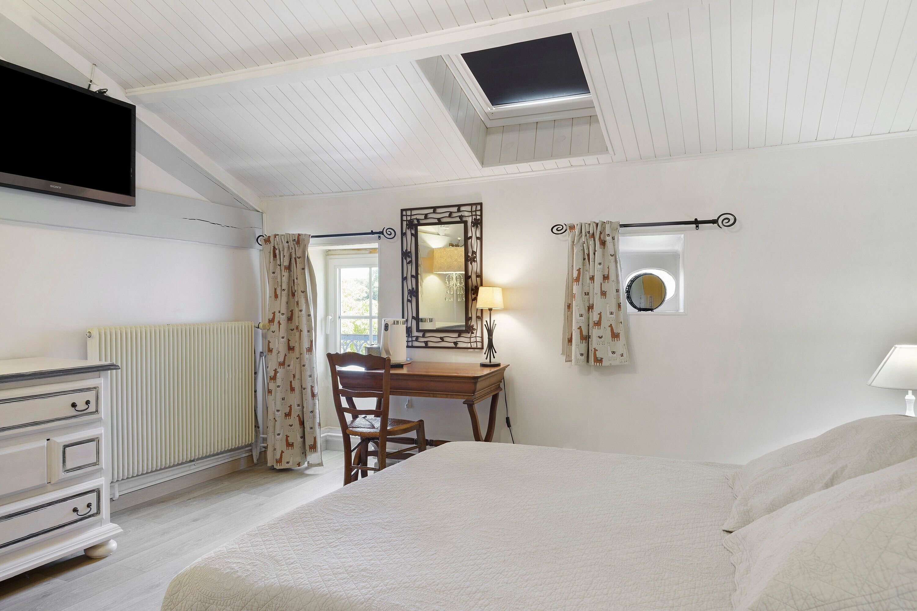 Een slaapkamer met een bed, een bureau, een stoel, een dressoir, een spiegel en een televisie.