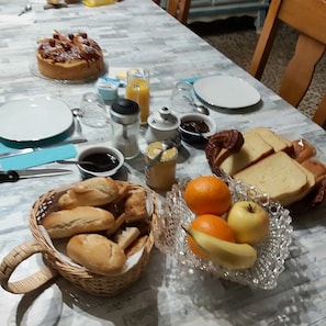 A breakfast table with bread, pastries, fruit, and condiments.