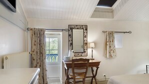 Quarto com cama, escrivaninha, cadeira, radiador, janela com cortinas e espelho na parede.