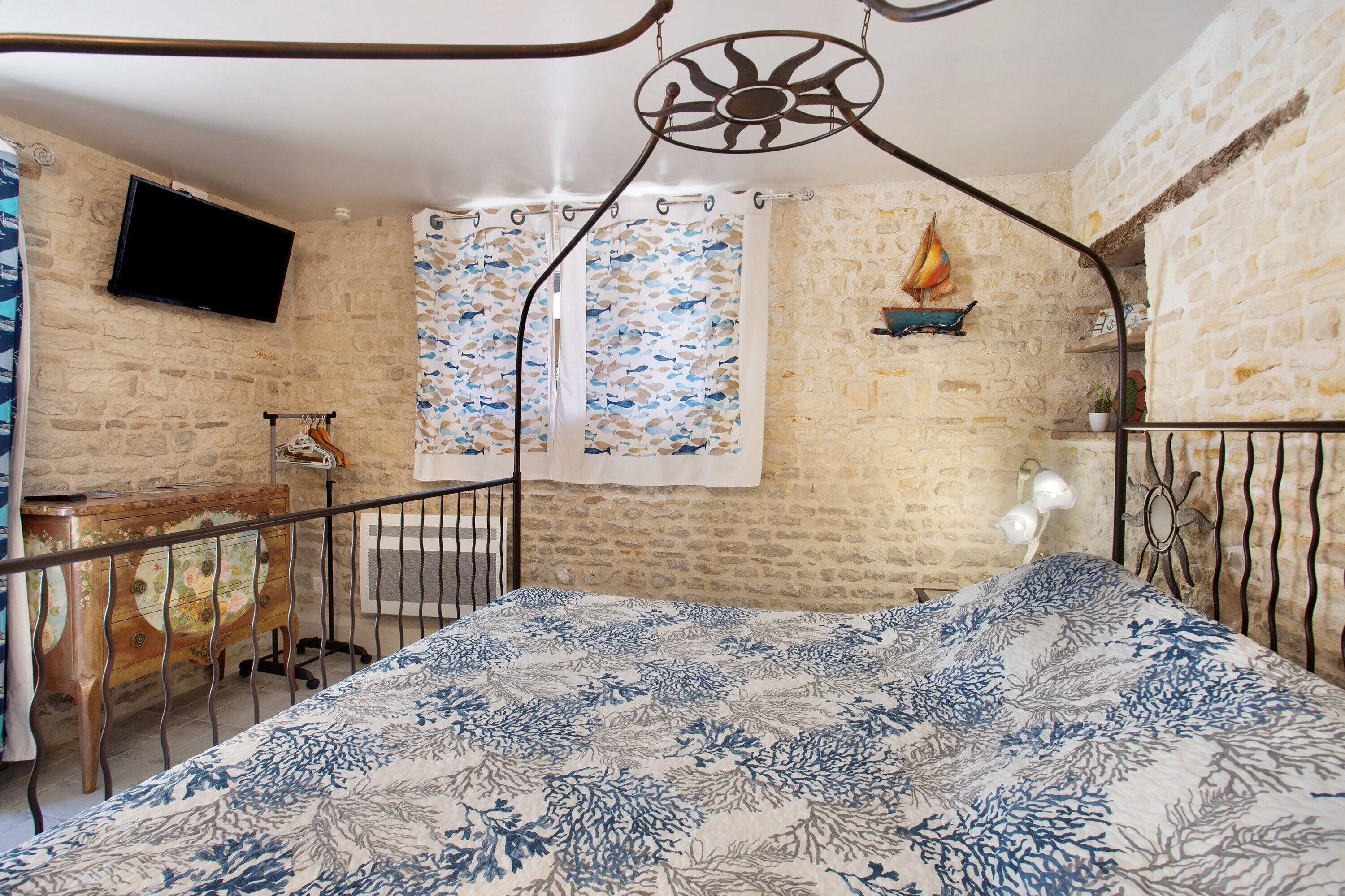 A bedroom with a bed, a TV, a wooden dresser, and a stone wall.