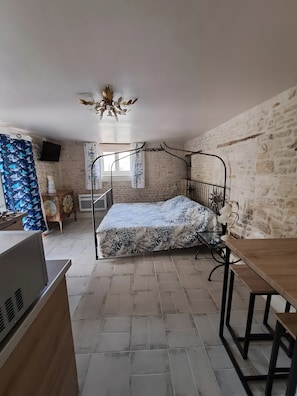 Un dormitorio con cama, escritorio, silla, televisor y pared de piedra.