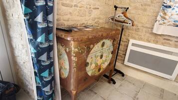 Eine rustikale Steinwand, ein Holzschrank mit floralen und Segelbootmotiven, eine Heizung und ein Vorhang mit Bootsdesigns.