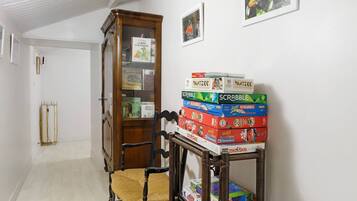 Een hal met een houten stoel, een boekenplank en een stapel gezelschapsspellen.