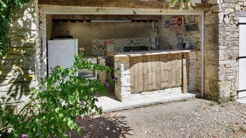 Una cucina esterna rustica con un muro in pietra, un bancone in legno e un frigorifero bianco.
