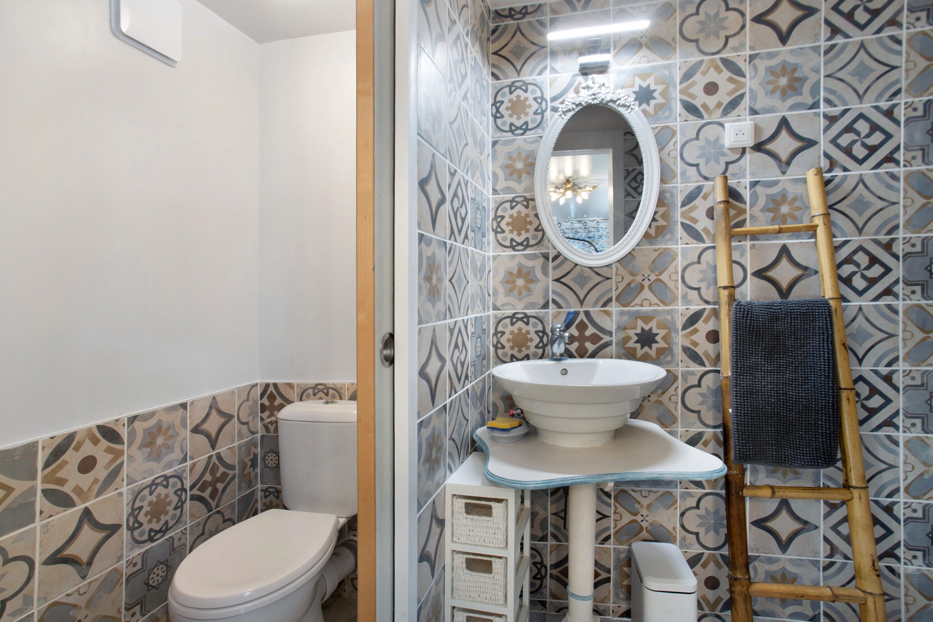Casa de banho com sanita, lavatório, espelho e azulejos estampados.