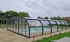 Una piscina techada con techo transparente, rodeada de grava y vegetación.