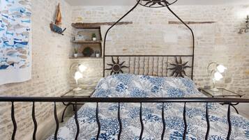 A bedroom with a stone wall, a metal bed frame, a patterned bedspread, and two bedside lamps.