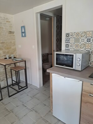 Una cocina compacta con microondas, un refrigerador pequeño, una mesa de madera y un salpicadero de azulejos.