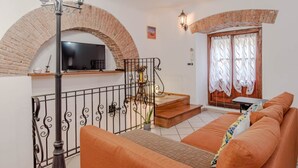 Un soggiorno con un arco in mattoni, una scala, un divano, una TV e una lampada.