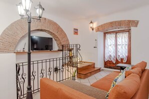 Un soggiorno con un arco in mattoni, una scala, un divano, una TV e una lampada.