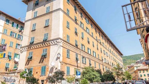 Un edificio a più piani con un ingresso angolare, ampie finestre e un'antenna parabolica ben visibile.