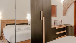 Una camera da letto con un letto di legno, un armadio scuro, una piccola scrivania con un portafoto e un arco in mattoni.