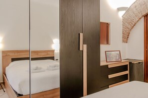 Una camera da letto con un letto di legno, un armadio scuro, una piccola scrivania con un portafoto e un arco in mattoni.